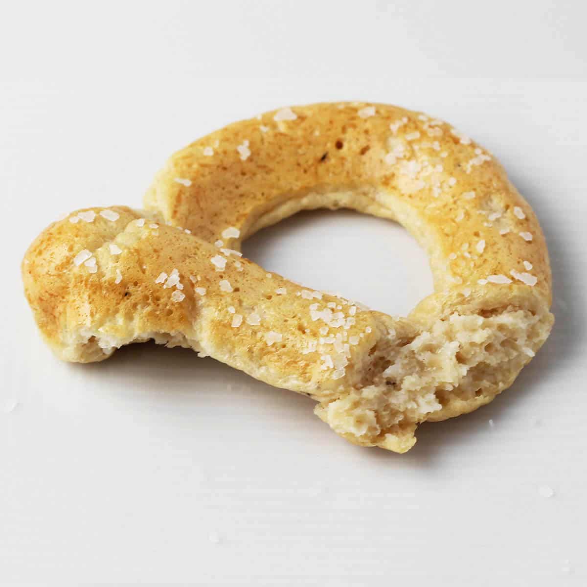 partially eaten protein pretzel with coarse salt on a white plate