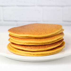 a stack of pumpkin protein pancakes on a white plate with a white table and white brick background
