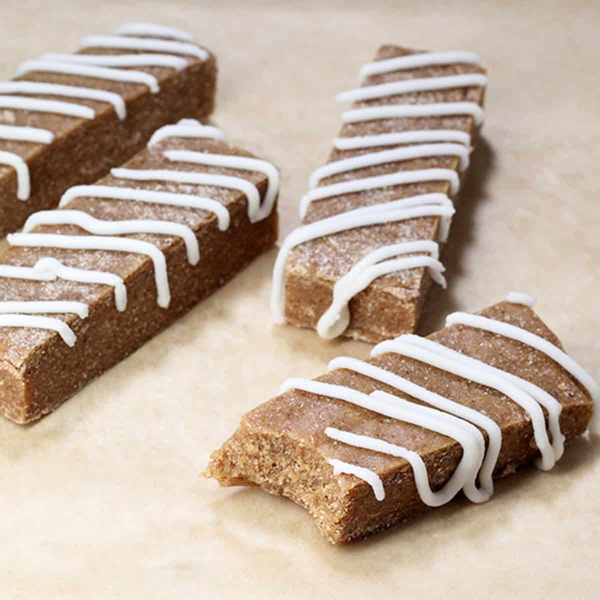 four protein bars, one bitten, that are apple pie flavor with white icing on a sheet of unbleached parchment paper