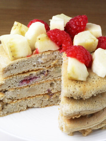 a stack of fluffy protein pancakes with bananas and raspberries inside the pancakes and on top of the pancakes