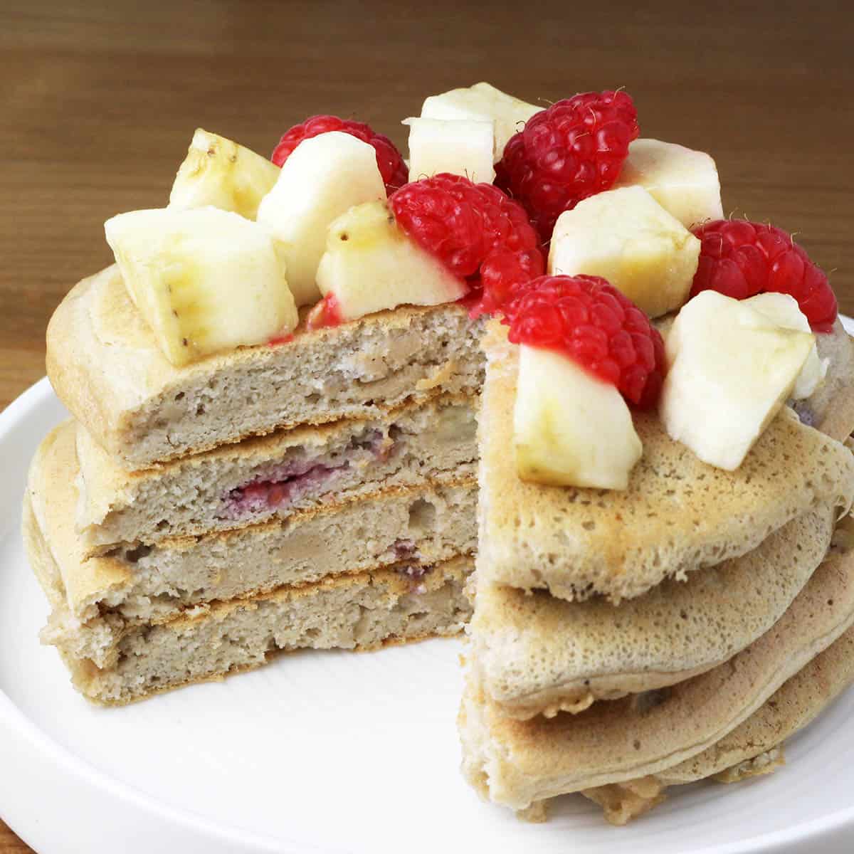 a stack of fluffy protein pancakes with bananas and raspberries inside the pancakes and on top of the pancakes