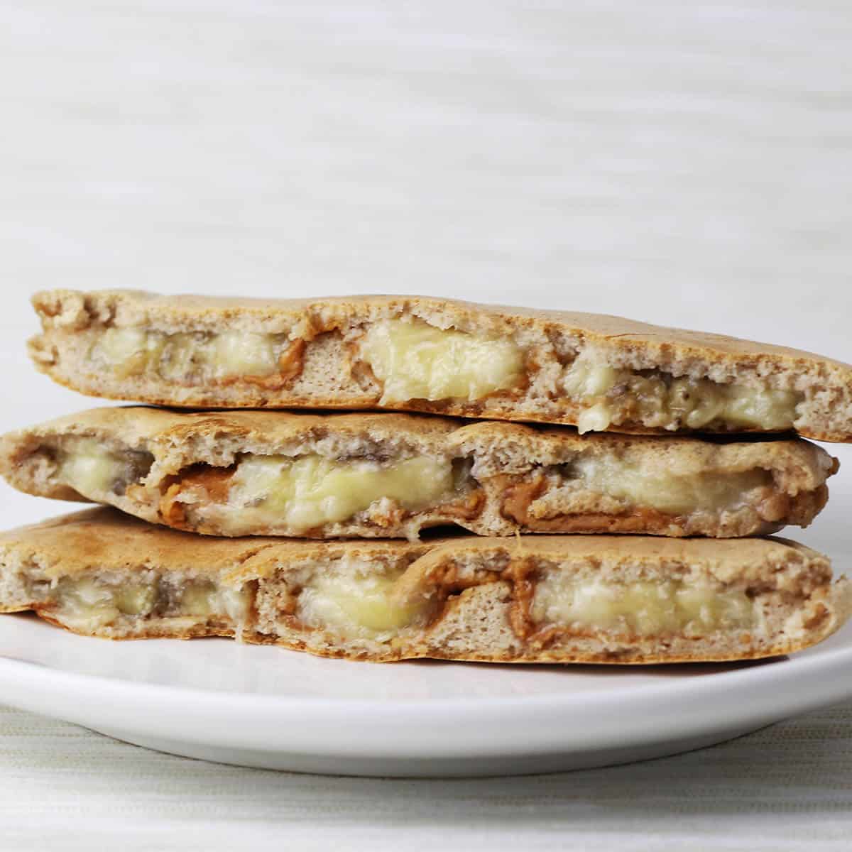 stacked halves of stuffed protein pancakes with visible banana and peanut butter inside each pancake half on a white plate with a light background