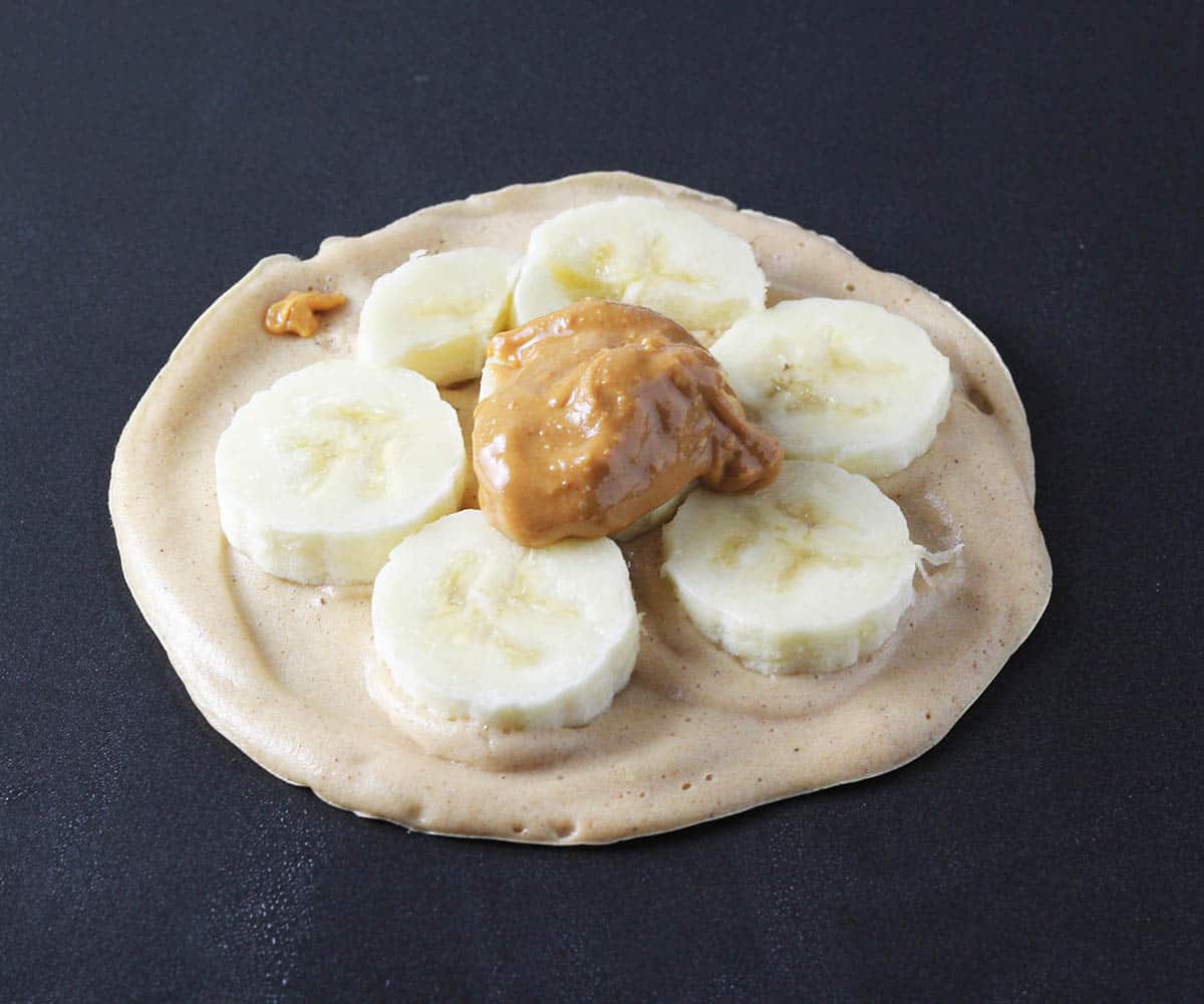 stuffed pancake process shot- bottom layer of pancake topped with banana slices and a dollop of peanut butter on griddle