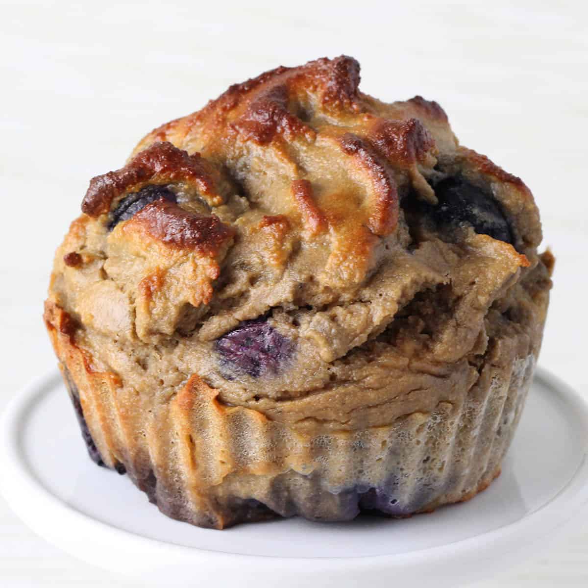 one large blueberry protein muffin on a white cupcake stand with a light background