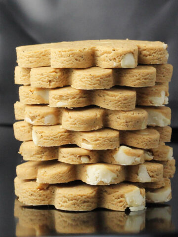 a stack of eight flower shaped cashew butter cookies on a dark background