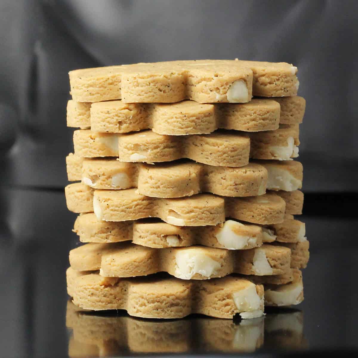 a stack of eight flower shaped cashew butter cookies on a dark background