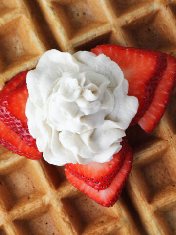 close up of a swirl of cashew whipped cream with strawberry slices on a low carb waffle