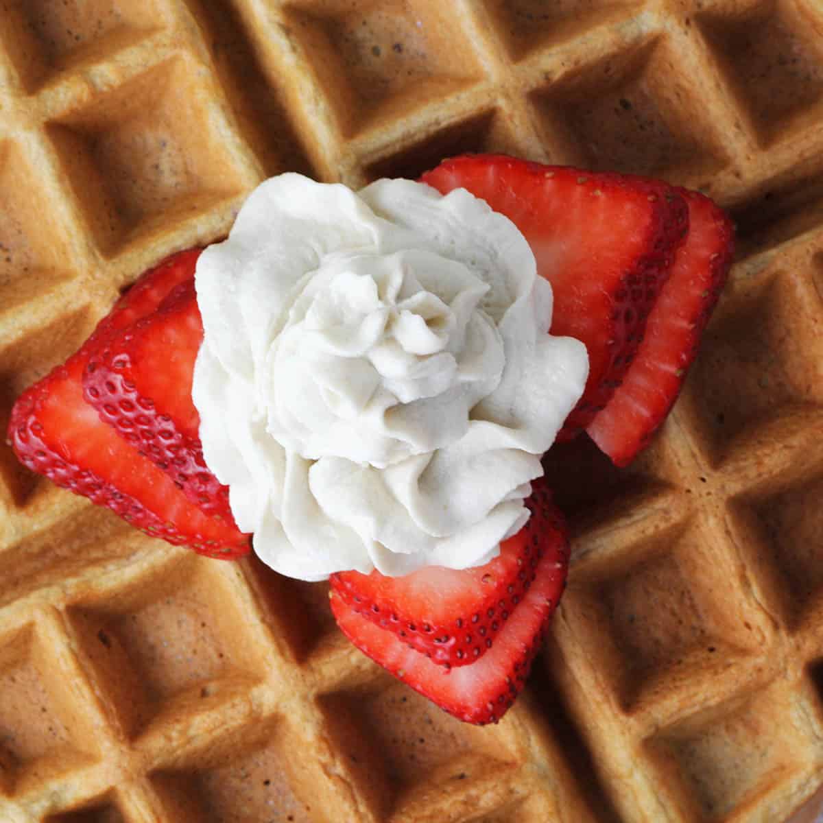 close up of a swirl of cashew whipped cream with strawberry slices on a low carb waffle