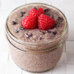 a small jar filled with chocolate chia pudding and topped with raspberries and cacao nibs