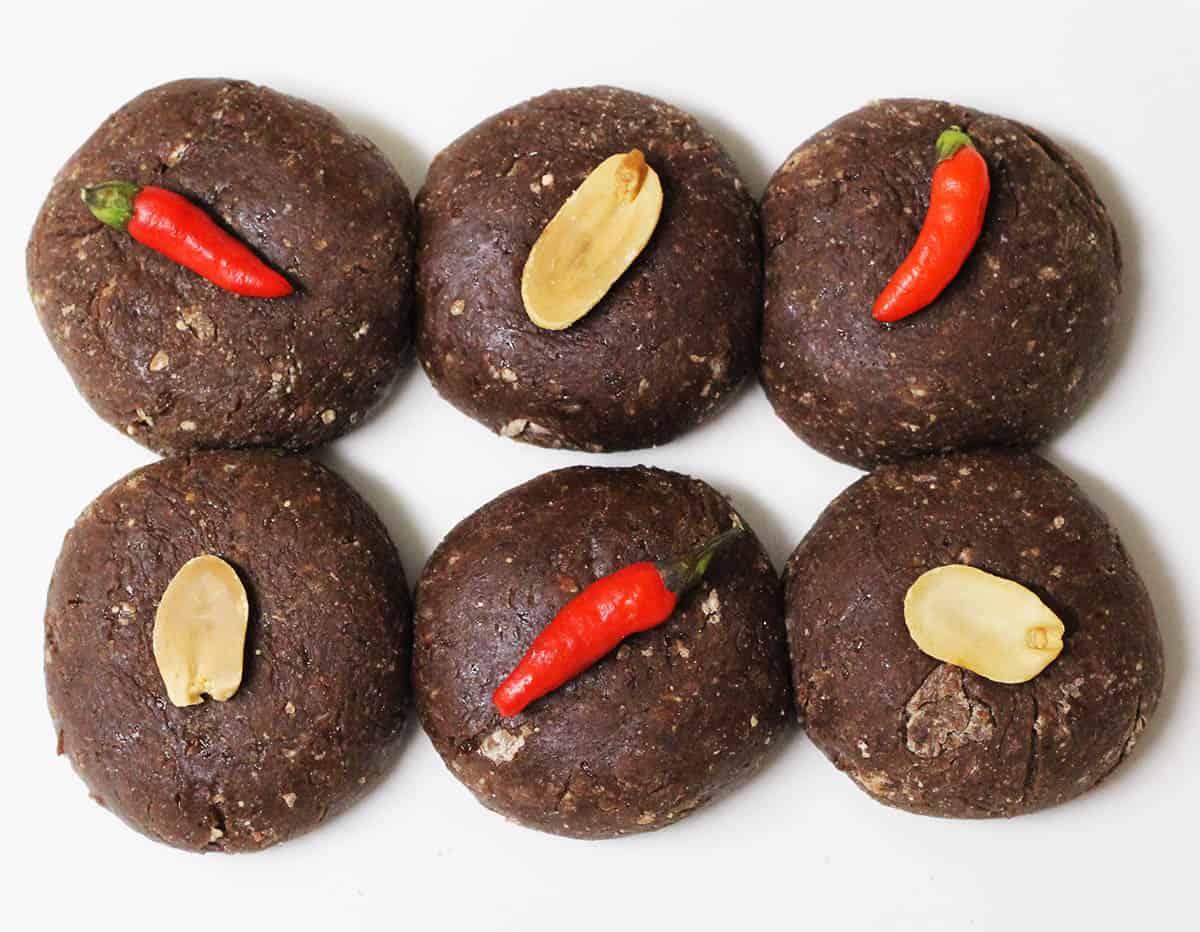 six chocolate chili protein balls with one of them bitten, with peanut halves and tiny red peppers on a white plate