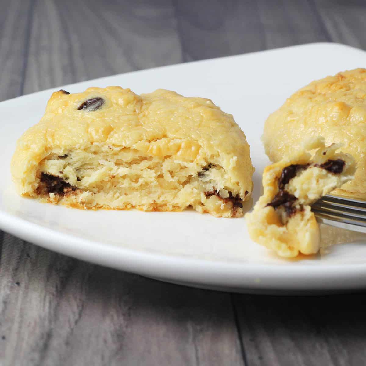 inside view of a soft baked chocolate chip protein cookie with a fork with a piece of cookie on it on a white plate on a grey background