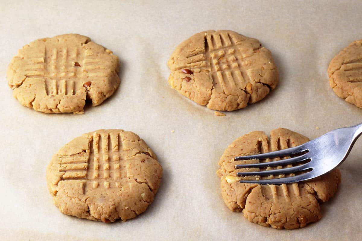 unbaked peanut butter protein cookies with a fork one one showing how to make the cross marks