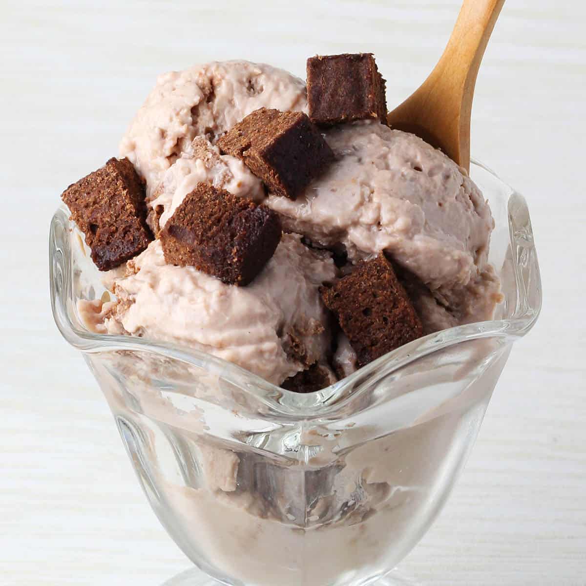 ice cream dish with chocolate fudge brownie frozen yogurt topped with chunks of protein brownie and a wooden dessert spoon