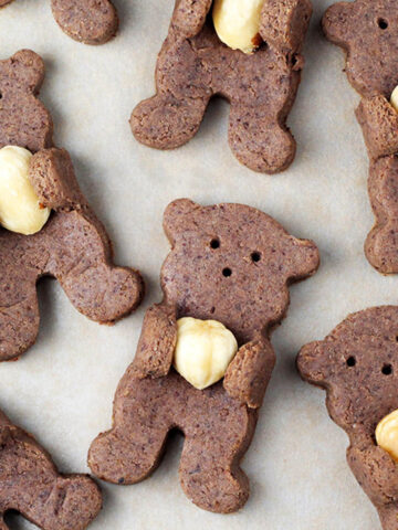 several chocolate teddy bear shaped cookies with their arms pulled up to hold a hazelnut