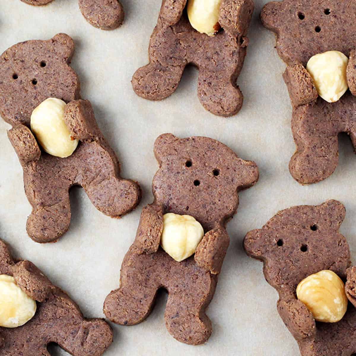 several chocolate teddy bear shaped cookies with their arms pulled up to hold a hazelnut