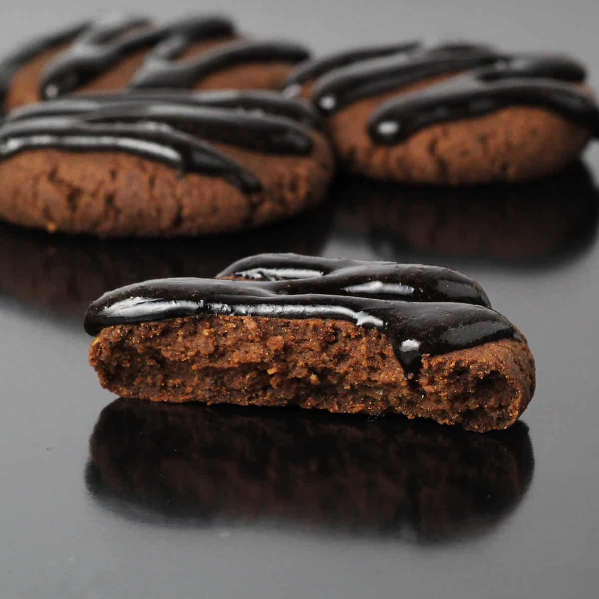 inside view of a chocolate hazelnut cookie drizzled with dark chocolate icing, with a few more cookies in the background and all on a black tray