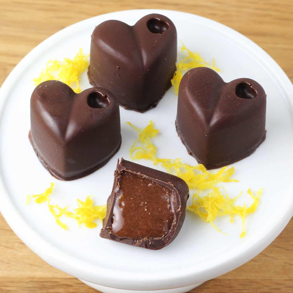 three full and one half chocolate heart filled with chocolate orange whey filling and orange zest on a small cupcake stand on a wood table
