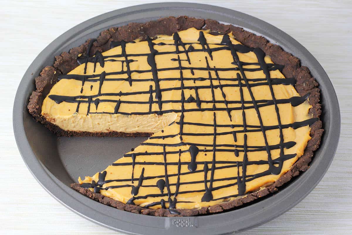 chocolate peanut butter pie with chocolate crust and chocolate drizzle with one slice missing in a metal pie dish with on a stainless steel counter