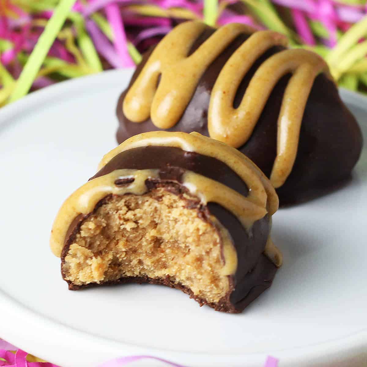 bitten chocolate covered protein peanut butter egg drizzled in peanut butter on a white plate and surrounded by colored paper shreds