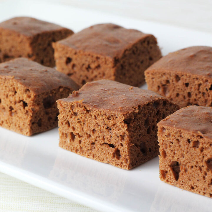 six pieces of square cut chocolate peanut butter protein snack cake on a white plate, side angled view