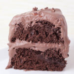 slice of double layer chocolate protein cake with fluffy chocolate protein frosting on a white background