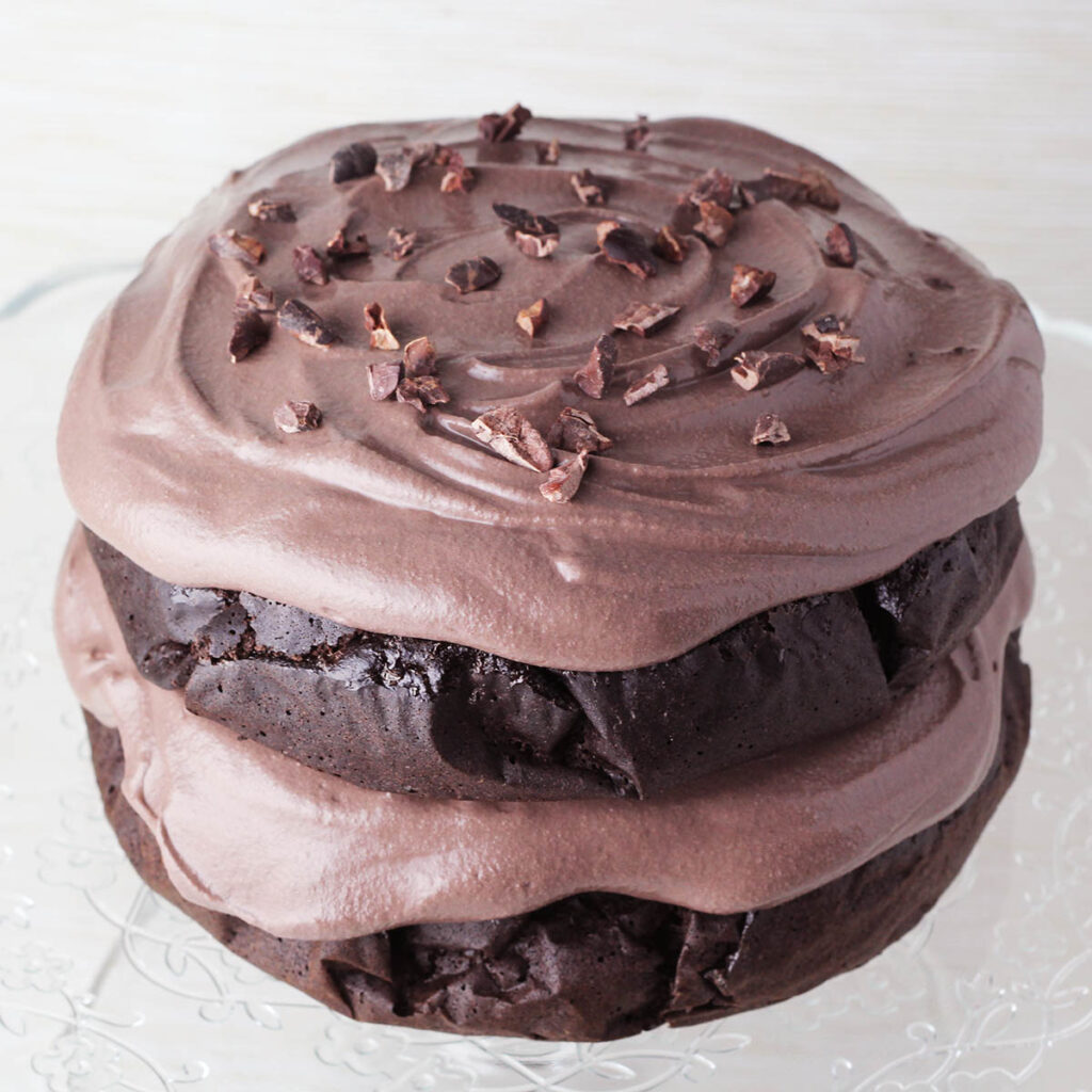 double layer round chocolate protein cake with fluffy chocolate protein frosting and topped with cacao nibs
