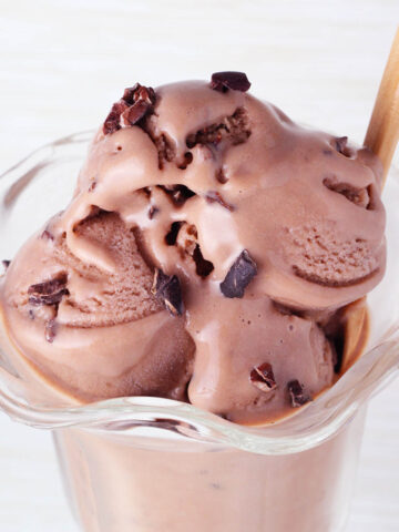 glass ice cream dish with chocolate protein ice cream topped with cacao nibs with a wooden dessert spoon