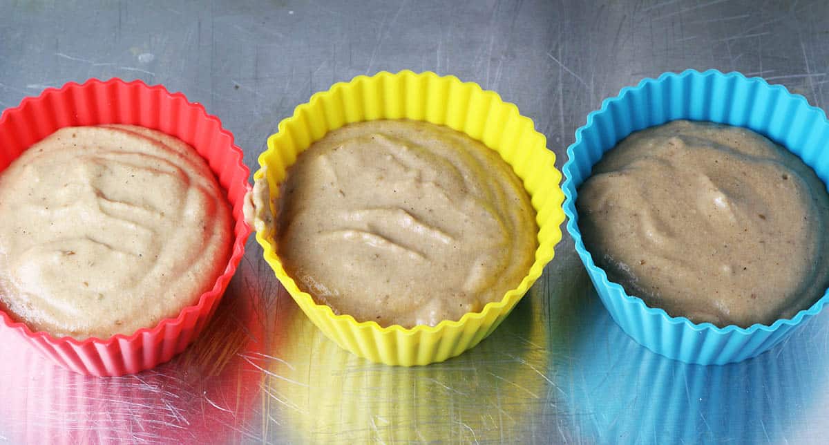 three large silicone muffin cups filled with batter on a silver baking sheet