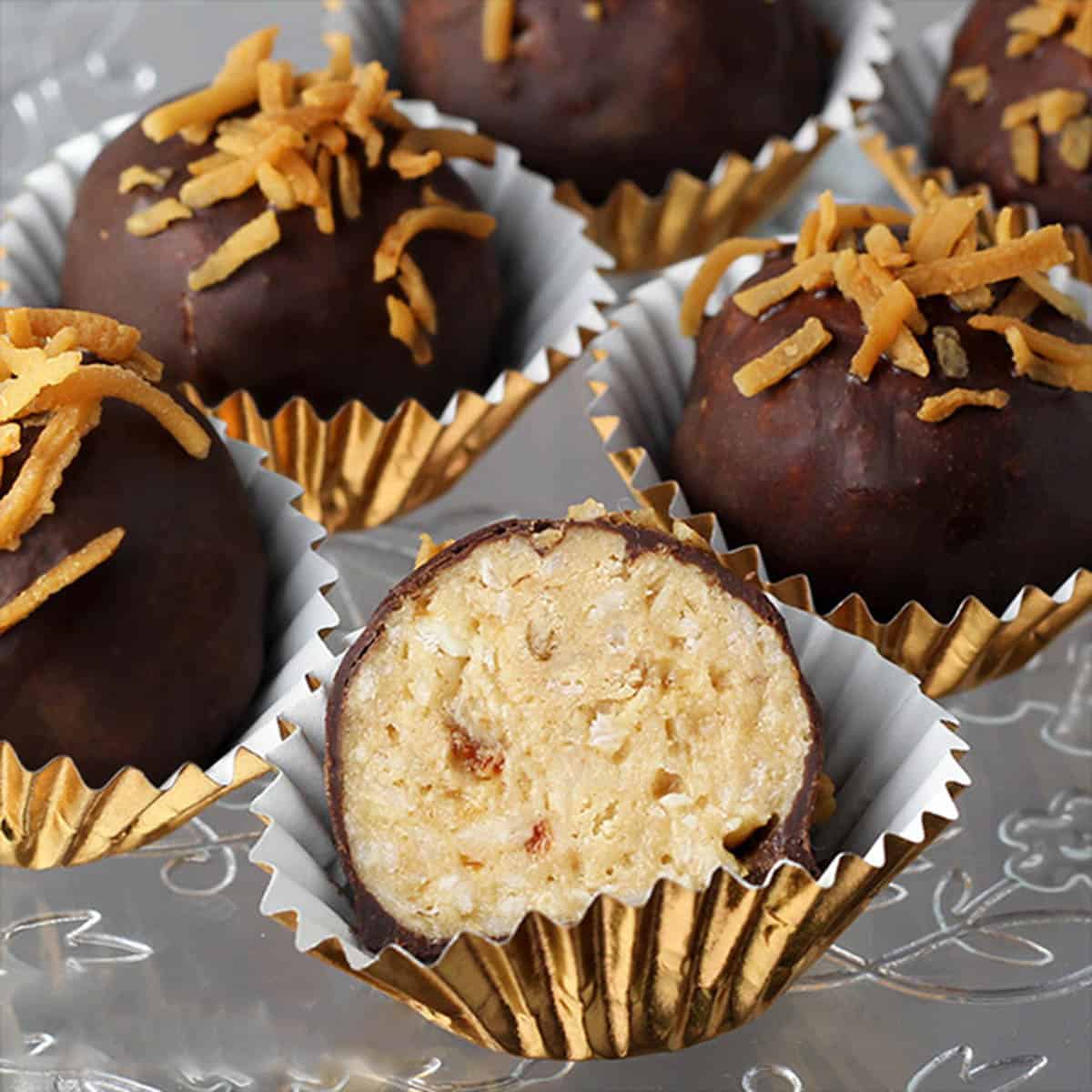 several full and one cut in half coconut caramel protein balls that are covered in chocolate and sprinkled with toasted coconut, each in a gold paper cup