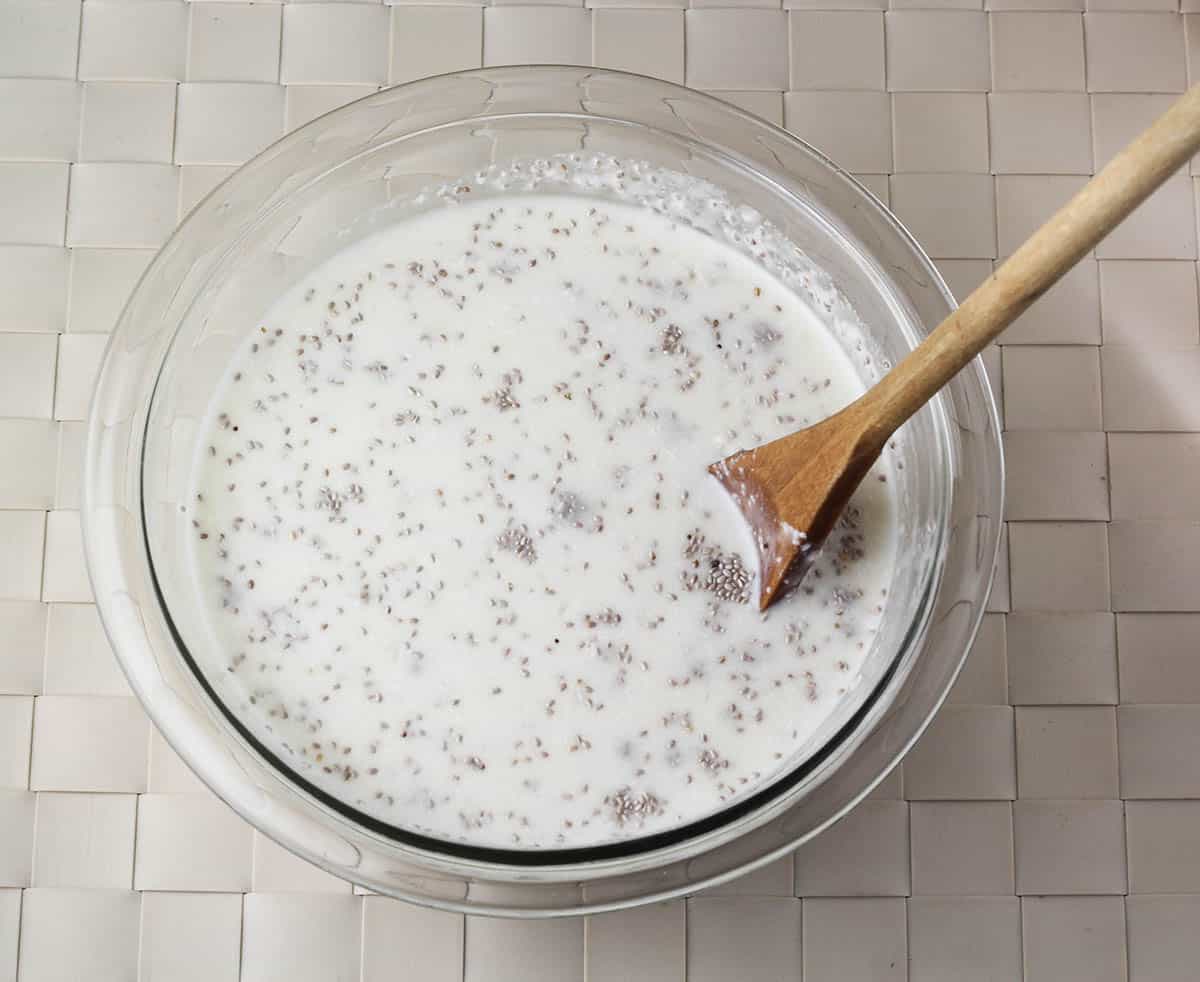 bowl of coconut chia pudding before it turns to pudding, glass bowl on woven beige placemat