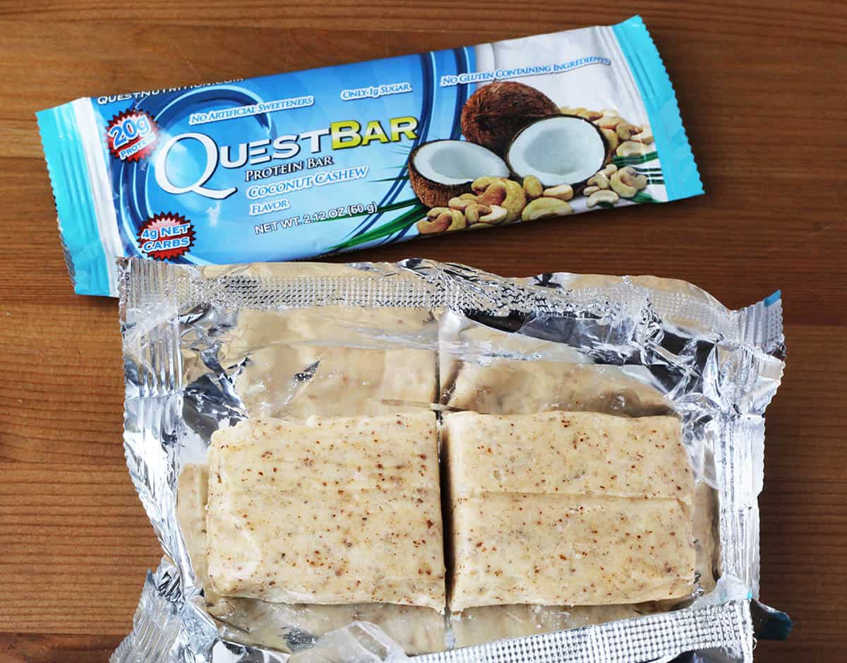 two coconut cashew quest bars, one unwrapped and cut into two pieces