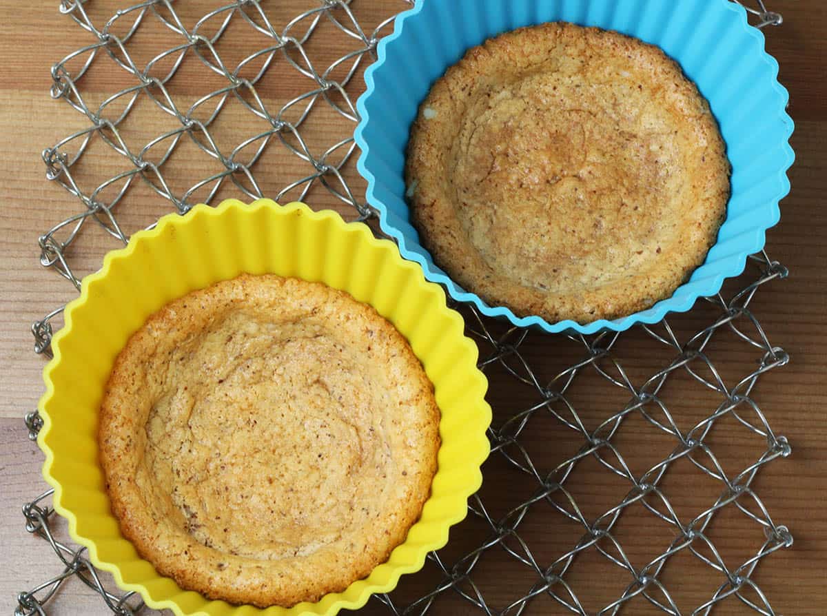 two large silicone muffin cups with quest bar baked into them as crust on a silver mesh trivet on a wood table