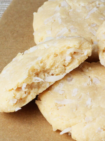inside view of a coconut protein cookie with visible coconut shreds and next to a few full cookies
