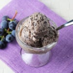 small glass dessert dish with a few scoops of grape gelato on a purple linen and with a small bunch of purple grapes