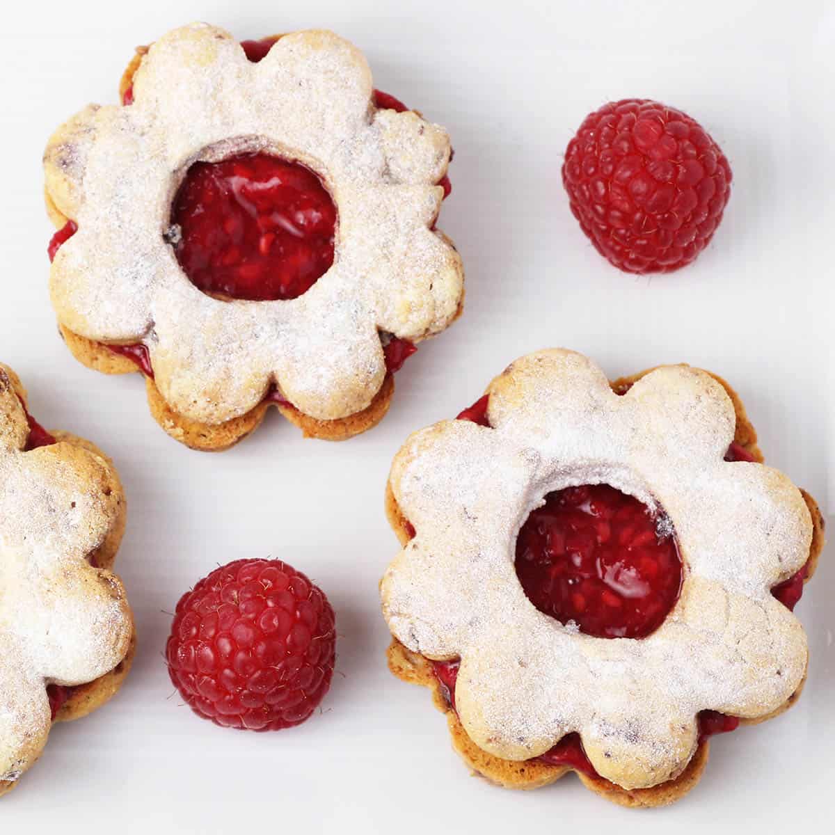 overhead view of linzer cookies shaped like flowers with fresh raspberries on a white plate