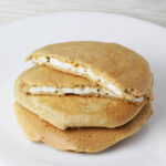 a stack of three egg white stuffed protein pancakes with the top one cut in half and the inside egg whites showing