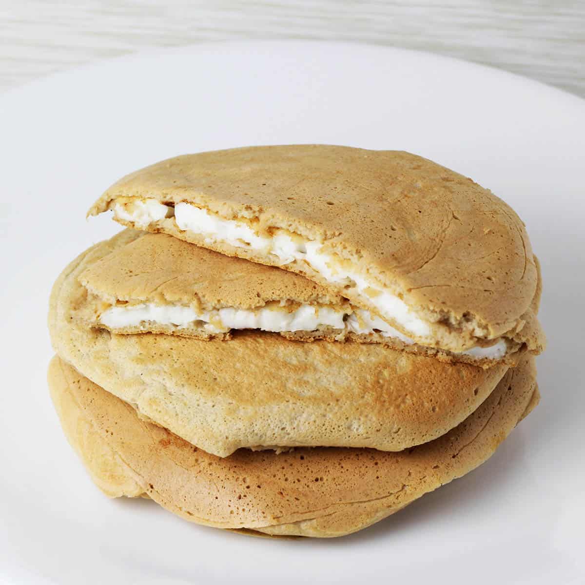 a stack of three egg white stuffed protein pancakes with the top one cut in half and the inside egg whites showing