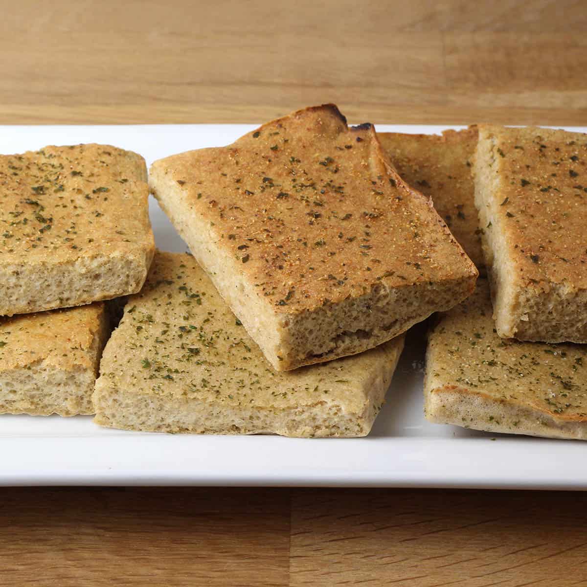 several pieces of garlic protein bread on a white plate on a wood table