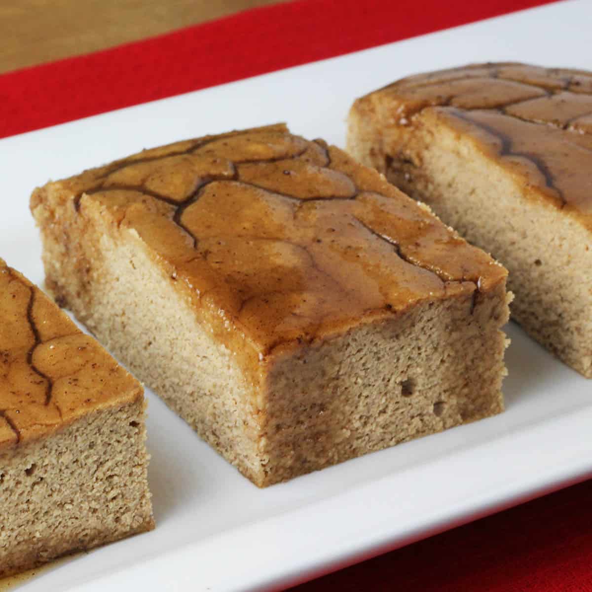 three pieces of maple glazed gingerbread protein cake on a white plate on a red napkin on a wood table