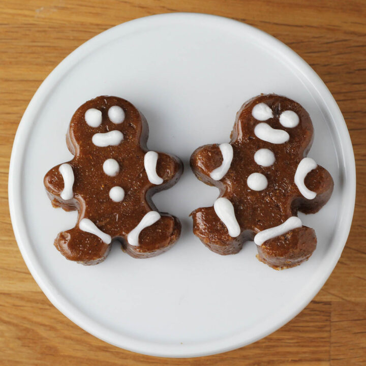 two iced gingerbread fudge pieces on a white cupcake stand on a wood table