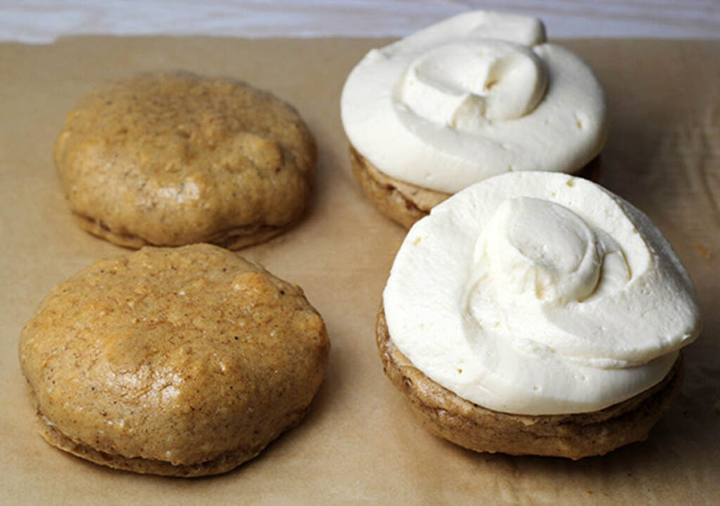 two gingerbread whoopie pie cookies without their tops on an unbleached sheet of parchment paper