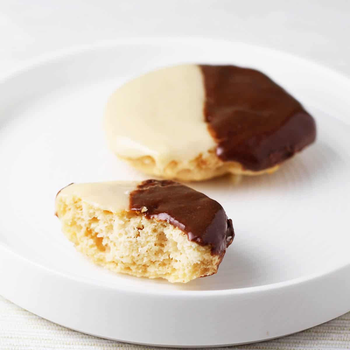 one bitten and one full mini black and white cookies on a white plate