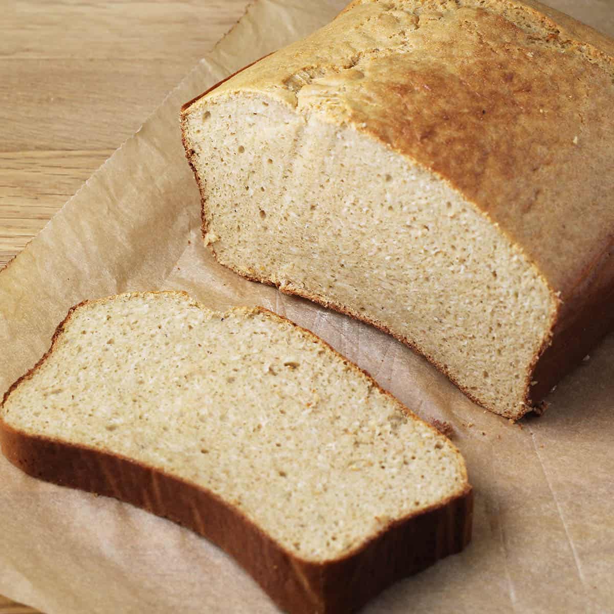 angled top view of a cut loaf of gluten free bread with one slice down in front on unbleached parchment paper on a wood table