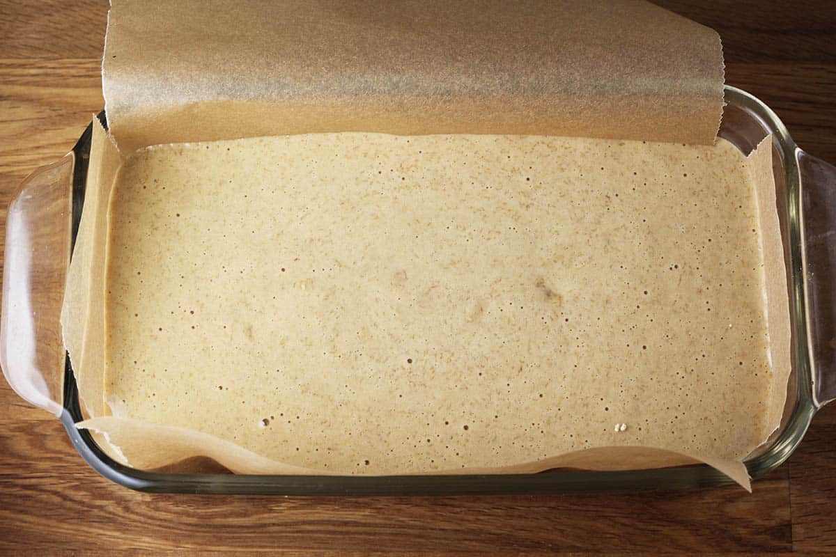 unbaked loaf of protein bread in a parchment lined glass loaf pan on a wood table