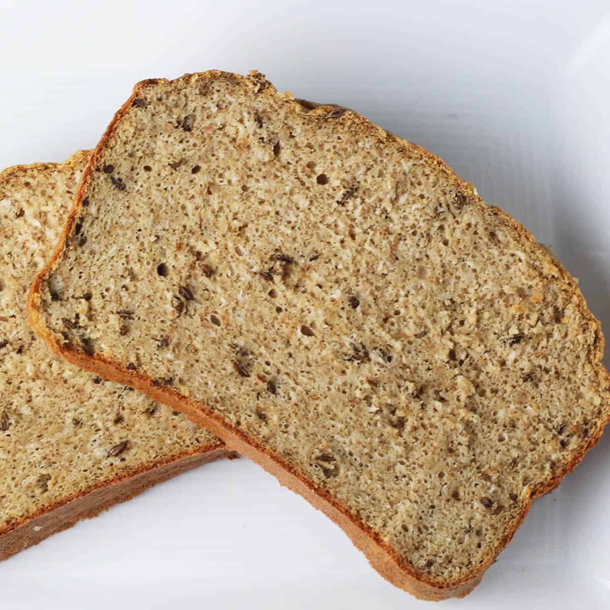 two slices of rye bread with caraway seeds on a white plate