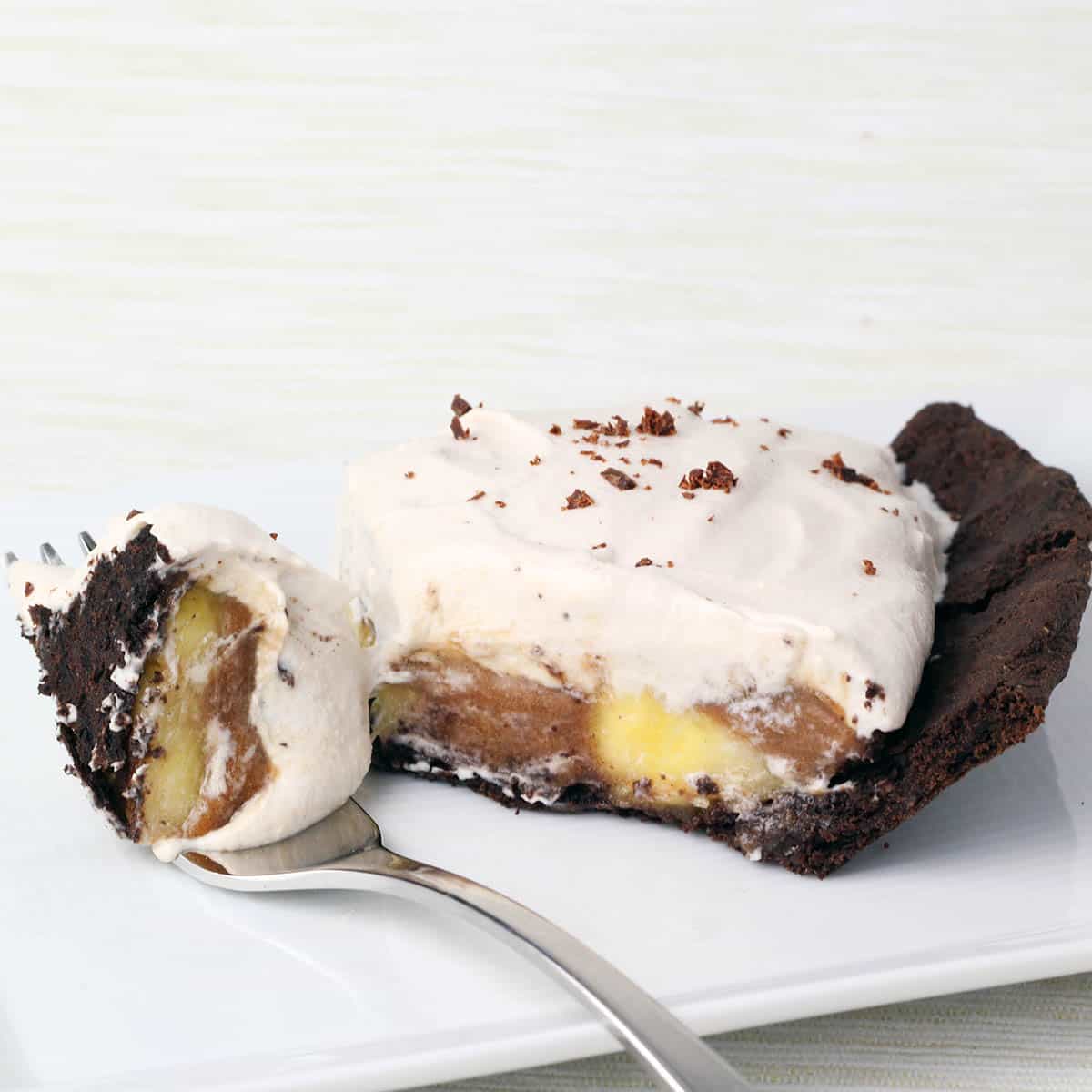 slice of banoffee pie showing the layers and with a forkful pulled from the slice, all on a white plate