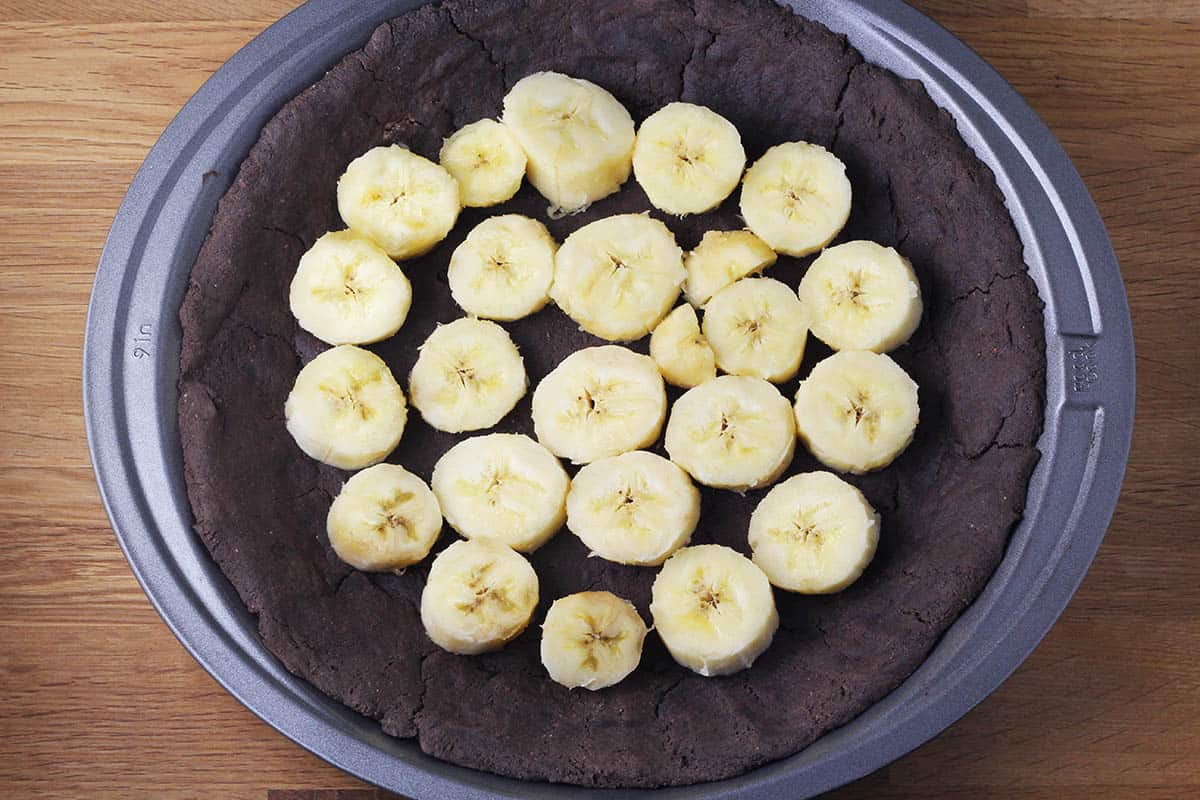 dark chocolate pie crust with banana slices in a metal pie pan on a wooden table