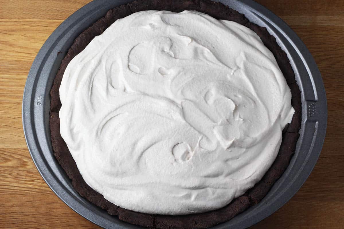 dark chocolate pie crust with filling and banana cashew whipped cream topping in a metal pie pan on a wooden table