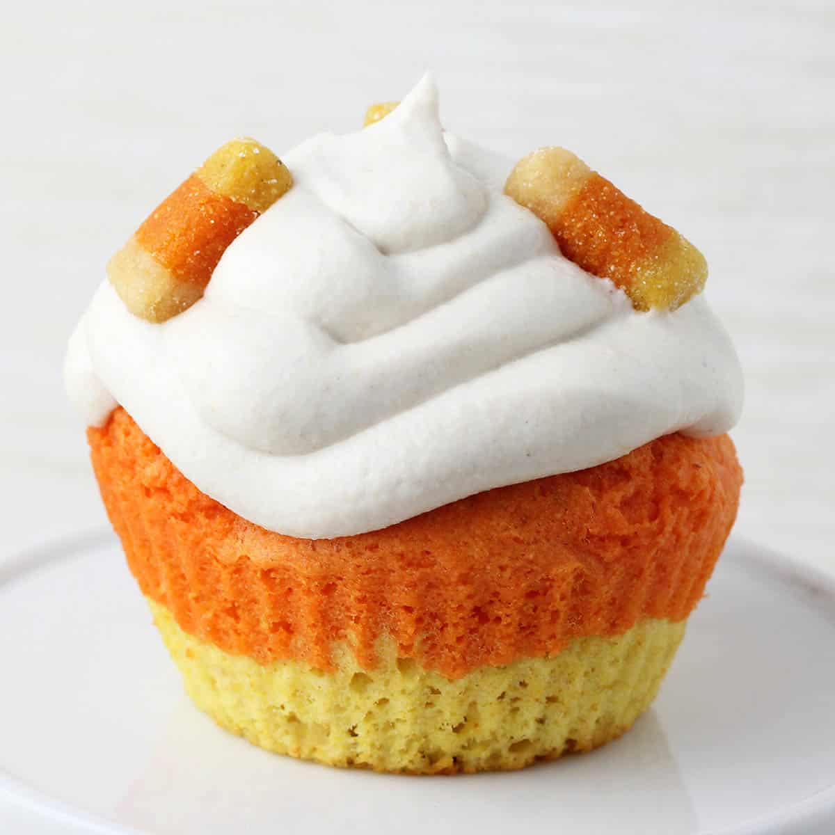 yellow and orange layered protein cupcake with white frosting and three pieces of protein candy corn on top