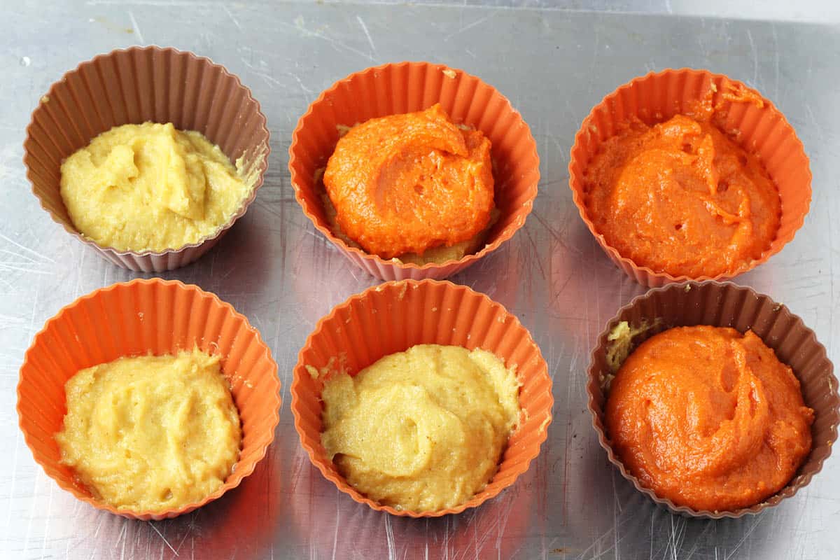 six silicone cupcake cups filled with yellow and orange protein cake batter in them